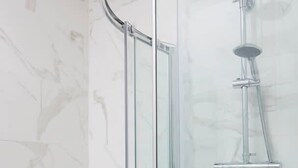 A glass-enclosed shower with a curved design, a chrome showerhead, and a visible water pipe.