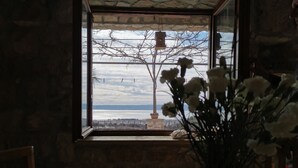 Une pièce dotée d’une grande fenêtre donnant sur un plan d’eau et sur un arbre. Un vase rempli de fleurs est posé sur une table au premier plan.