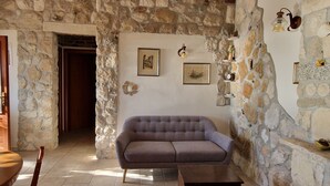 Une pièce aux murs de pierre, avec un canapé gris, une table en bois et un petit meuble en bois.