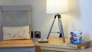 Une pièce chaleureuse avec une tête de lit en bois, une lampe sur un trépied, une tasse et une pile de livres sur une petite table.