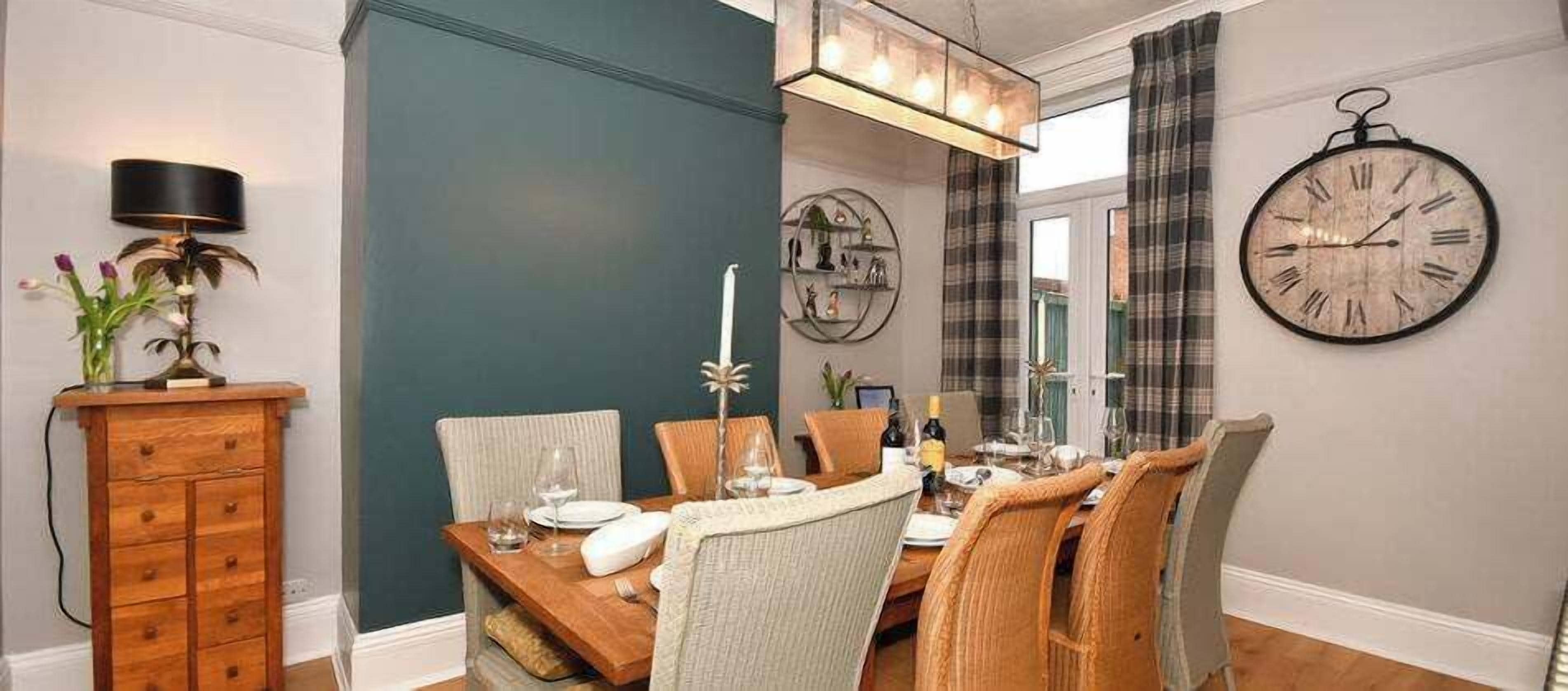 A dining area with a wooden table, chairs, a clock, and a lamp.