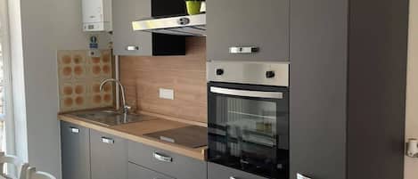 A modern kitchen with grey cabinets, a wooden countertop, a built-in oven, and a small window above the sink.