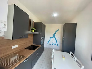 Una cocina compacta con armarios grises, una encimera de madera y una mesa de comedor blanca con sillas.