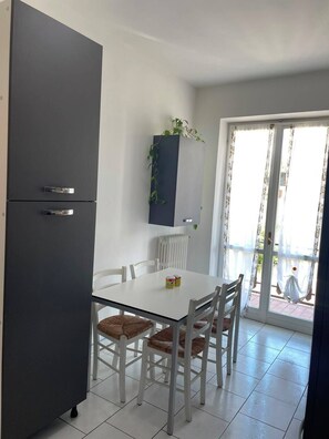 Un comedor con una mesa blanca, cuatro sillas, un armario gris y un ventanal con cortinas.
