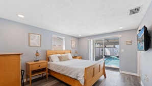 Une chambre avec un lit en bois, des tables de chevet, une armoire et une vue sur une piscine extérieure.