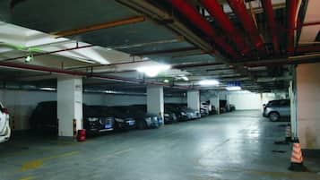 An underground parking garage with multiple rows of parked cars and visible structural elements like pillars and overhead pipes.