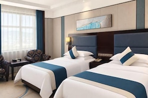 Habitación de hotel con dos camas, un escritorio, una silla, una ventana con cortinas y un cuadro en la pared.