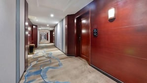 Un couloir d'hôtel avec un sol recouvert de moquette, des murs en bois et une série de portes donnant sur les chambres.
