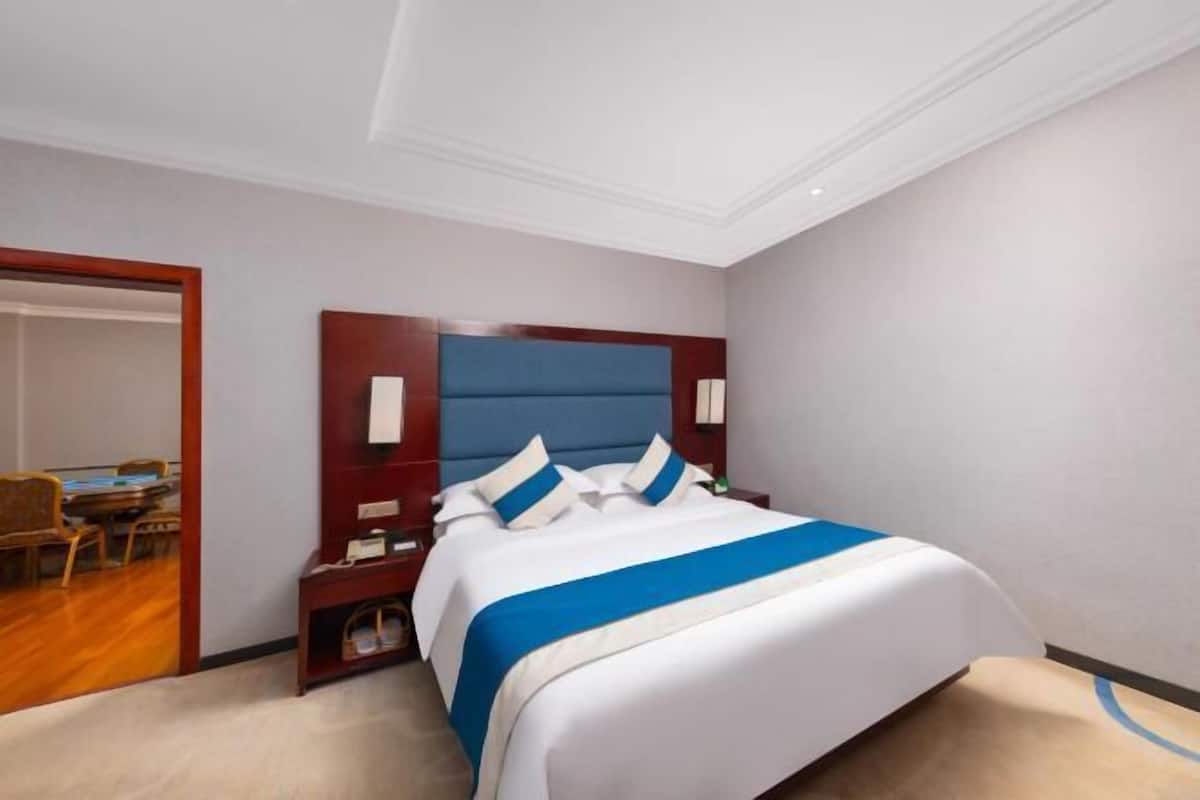 A hotel room with a large bed, a wooden headboard, a nightstand, and a desk with chairs.