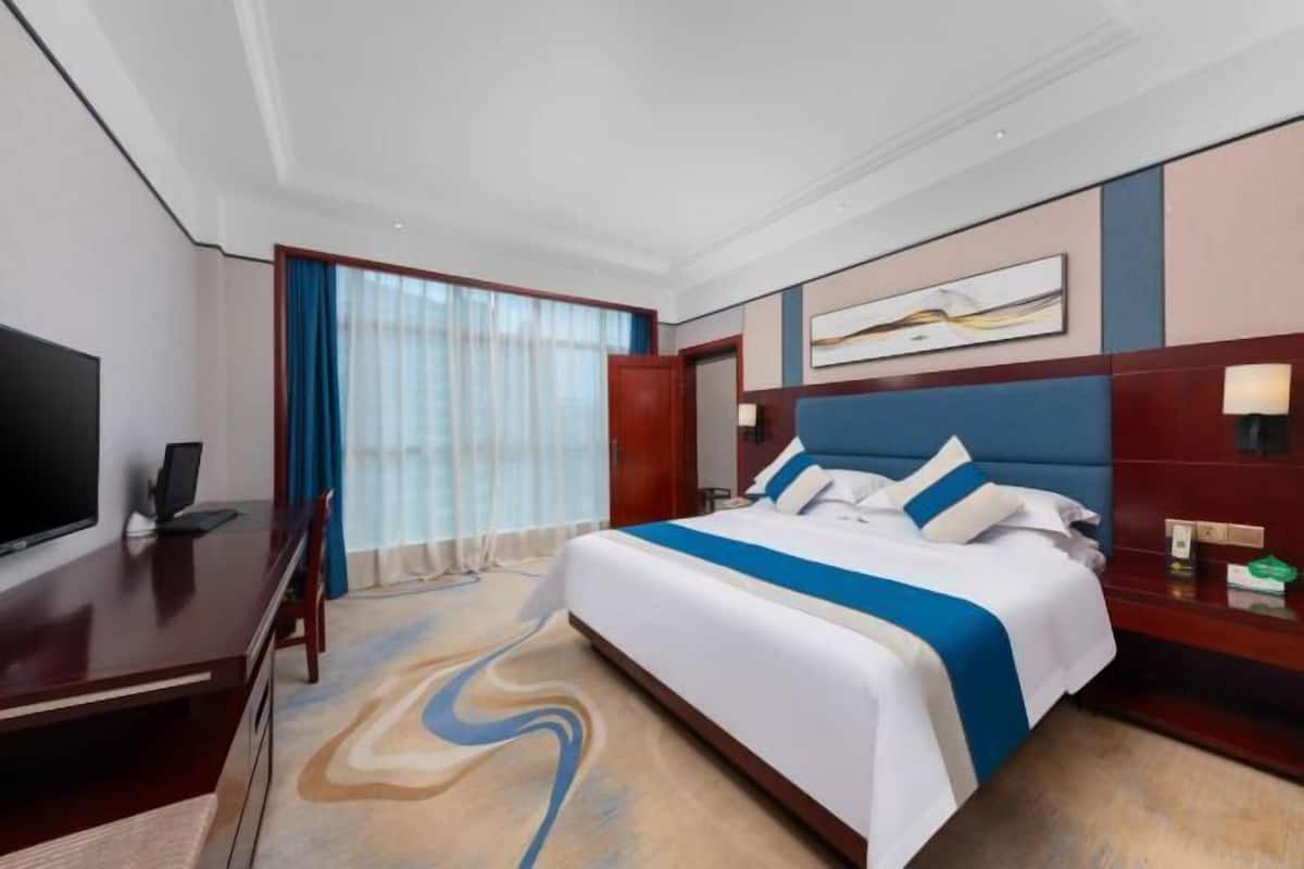 A hotel room with a large bed, a desk, a TV, and a window with curtains.