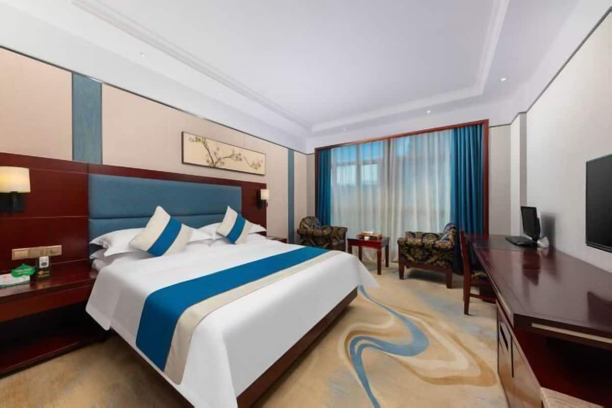 A hotel room with a large bed, a desk, a chair, a TV, and a window with curtains.