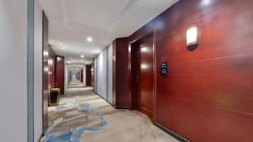 A hotel hallway with a carpeted floor, wooden walls, and doors leading to rooms.