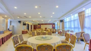 A spacious banquet hall with round tables and chairs, a stage, and large windows.