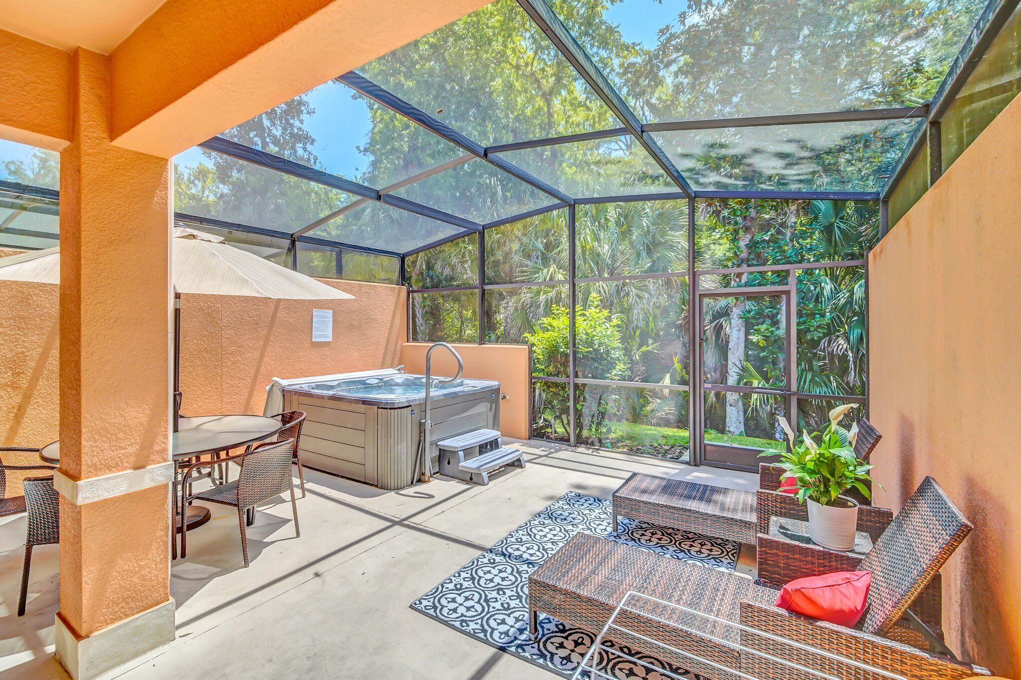 A covered patio area with a hot tub, outdoor seating, and a view of lush greenery.