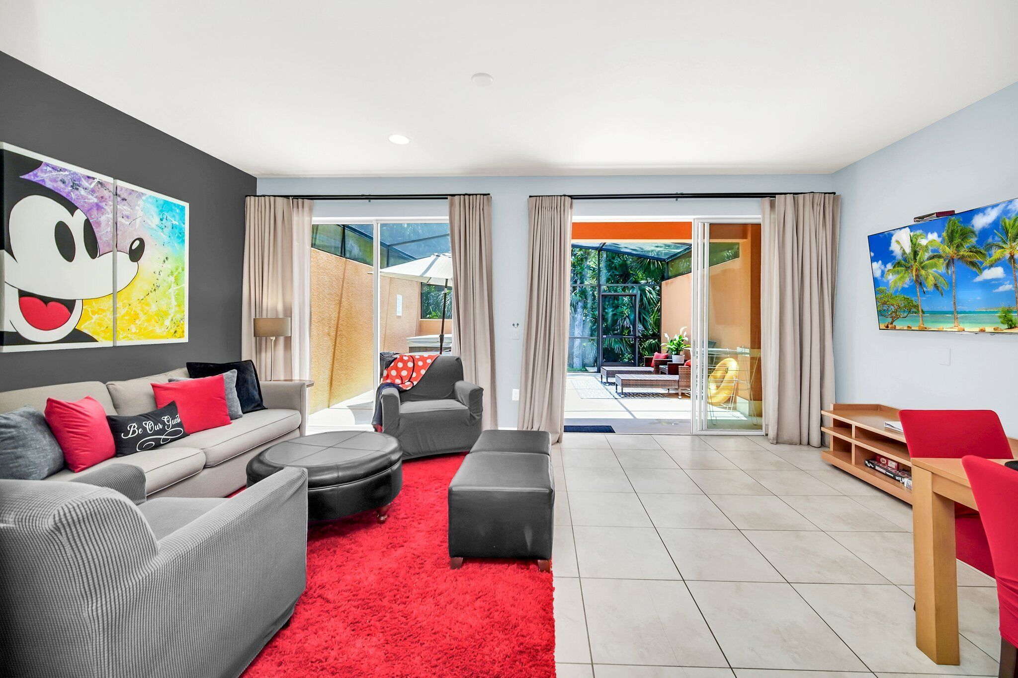 A modern living room with a grey sofa, red cushions, a red rug, and a large cartoon print on the wall.
