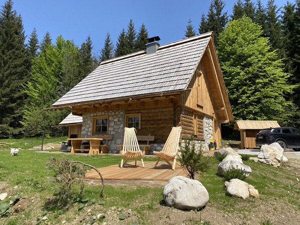 Une cabane en rondins avec des fondations en pierre, une terrasse en bois et un espace extérieur aménagé pour s’asseoir.