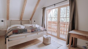 Une chambre avec un lit en bois, une fenêtre avec des rideaux, une table en bois et un petit tapis.