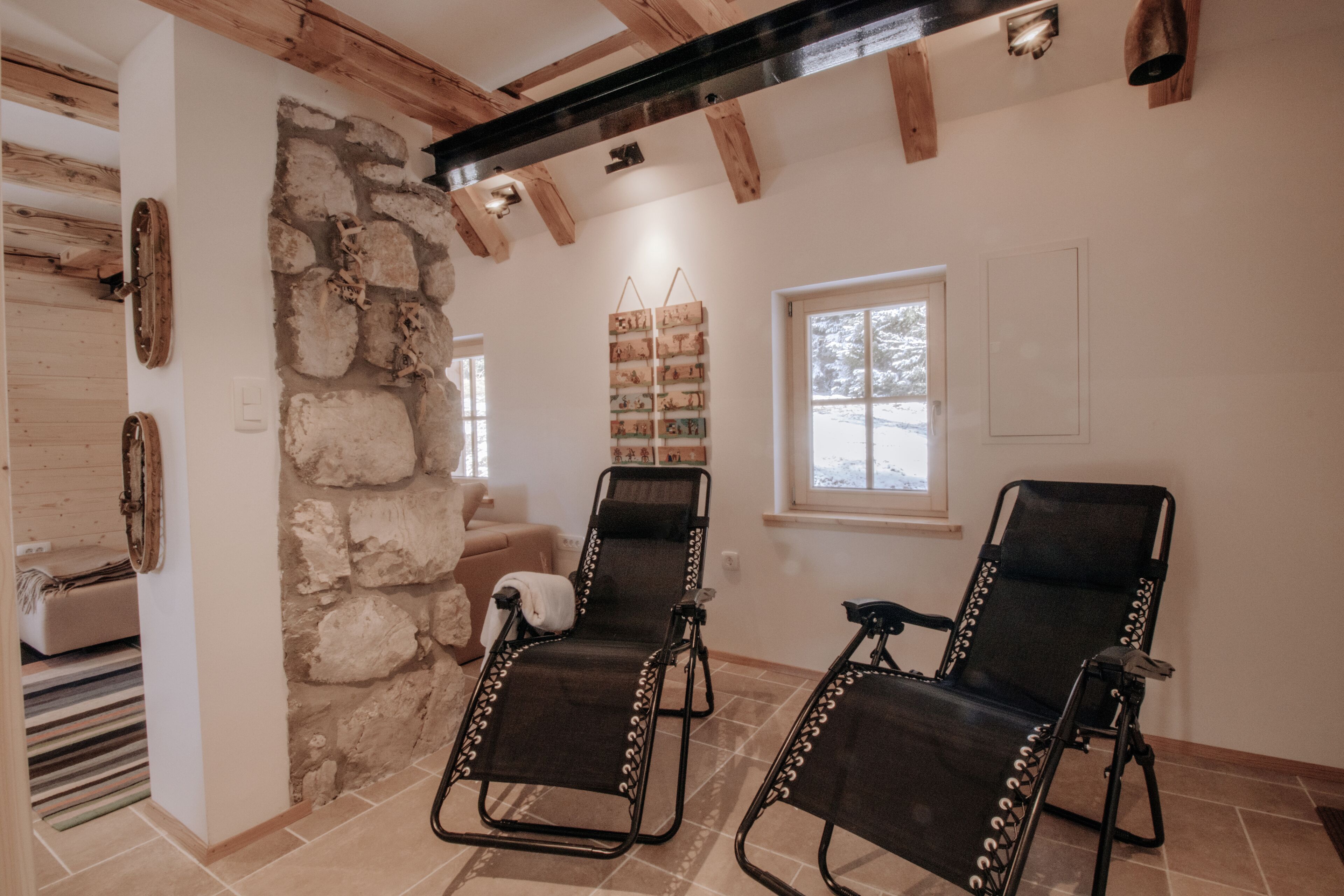A room with two reclining chairs, a stone wall, a window, and a wooden ceiling.