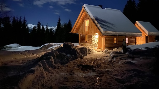 Une cabane en bois, avec un toit enneigé, des fondations en pierre et un revêtement extérieur en bois.