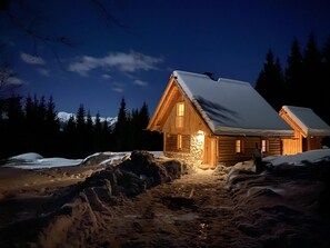 Une cabane en bois, avec un toit enneigé, des fondations en pierre et un revêtement extérieur en bois.