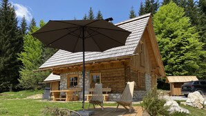 Une cabane rustique en rondins de bois, avec des fondations en pierre, une terrasse en bois et un espace salon extérieur.