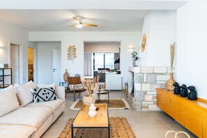 A modern living room with a sofa, coffee table, and decorative items. There is a kitchen in the background with a dining area. - MyKosVilla with private pool (Kos)