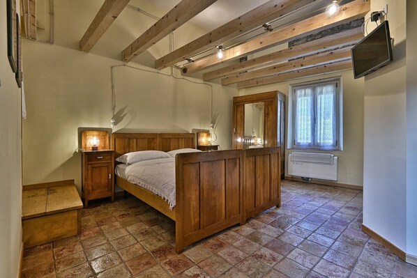 Un dormitorio con cama de madera, lámparas de noche, un espejo grande, una ventana con cortinas y un televisor montado en la pared.