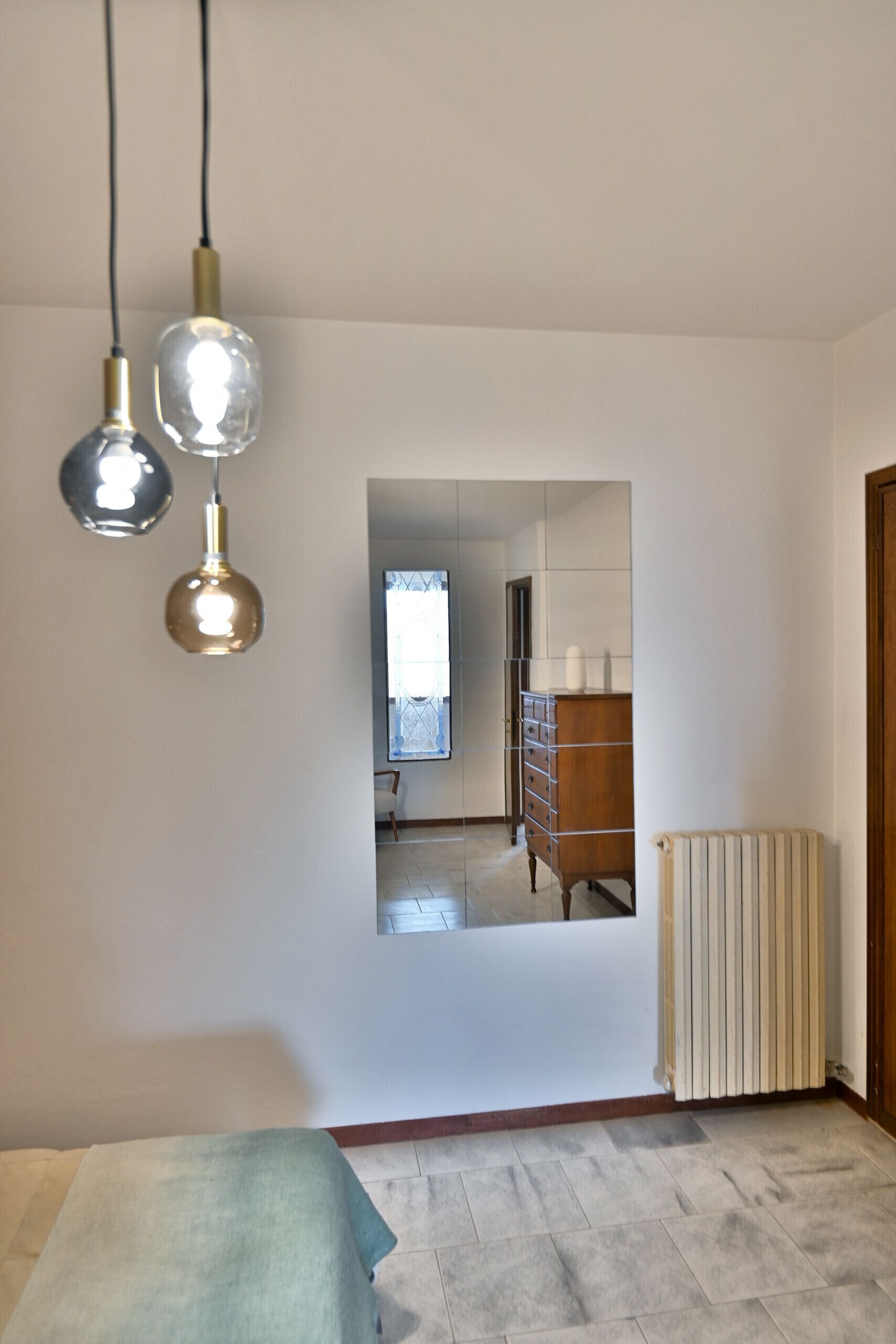 A room with a bed, a radiator, and a dresser. There are three hanging lights.