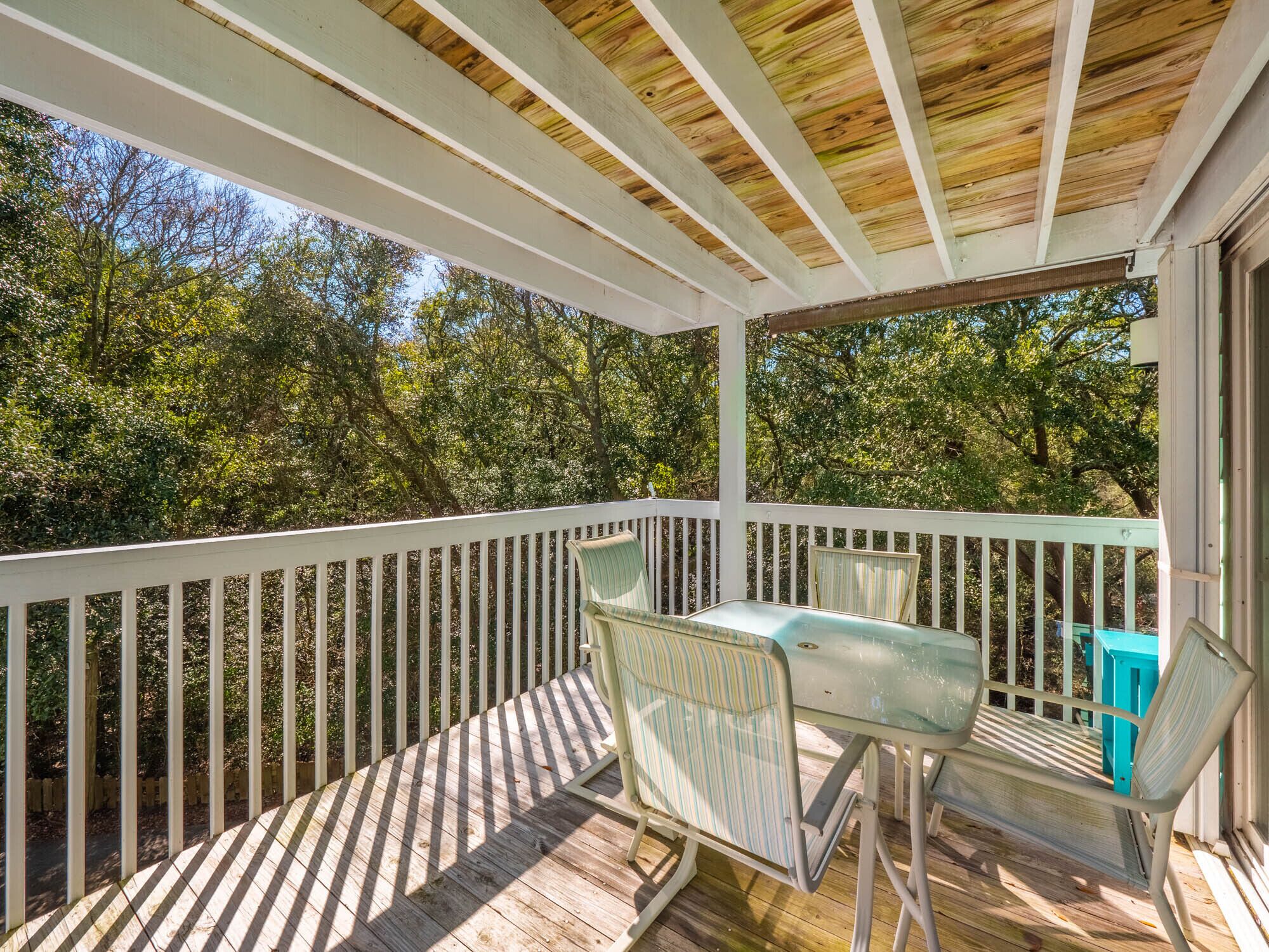 A covered outdoor deck with a white railing, two chairs, and a table.
