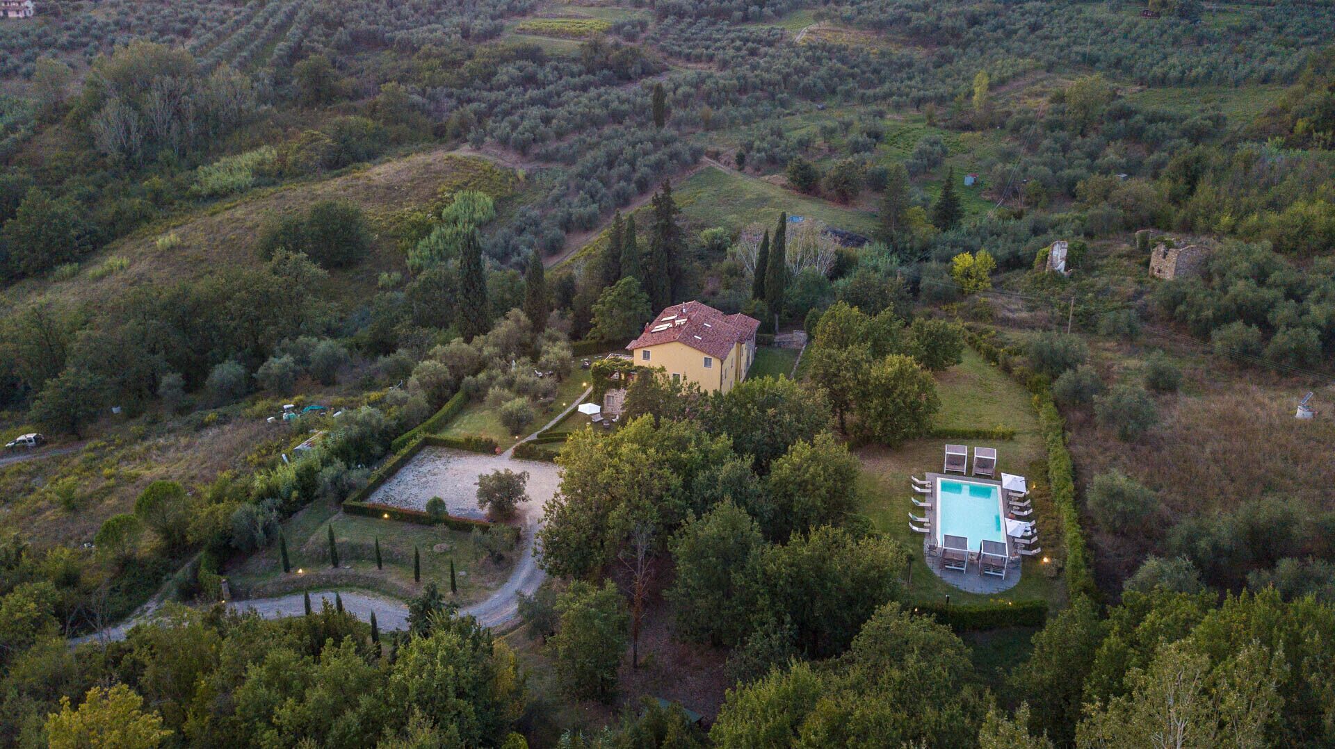 A villa surrounded by dense forest, with a swimming pool and a tennis court.