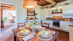 Une salle à manger bien éclairée, avec une table en bois dressée pour quatre personnes, entourée de chaises. On peut voir un luminaire suspendu au-dessus de la table.