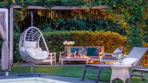 Un espace aménagé au bord de la piscine, avec un fauteuil suspendu, un canapé et une table décorée de bougies et de fleurs.