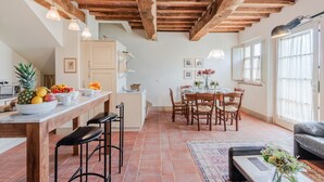 Eine geräumige Küche mit Holzbalkendecke, ein Essbereich mit Tisch für vier Personen und ein Wohnbereich mit Sofa und Couchtisch.