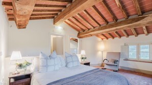 Ein Schlafzimmer mit Holzbalkendecke, einem Bett mit weißer Bettwäsche, einem Nachttisch, einem Stuhl und einem Fenster.
