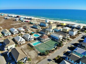 An aerial view of a coastal residential area with houses, a swimming pool, and a tennis court.
