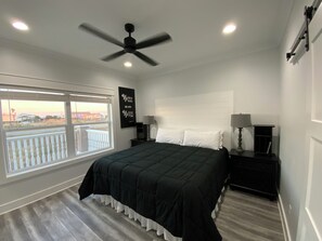 A bedroom with a large bed, two bedside tables, a ceiling fan, and a window with a view of buildings.