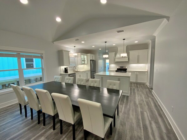 A modern kitchen with white cabinetry, a central island, and a dining area with a dark wooden table and white chairs.