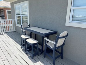 A patio with a table and four chairs, a white picket fence, and a building with a window.
