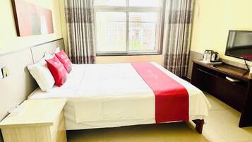 Een hotelkamer met een bed, bureau, televisie en raam met gordijnen.