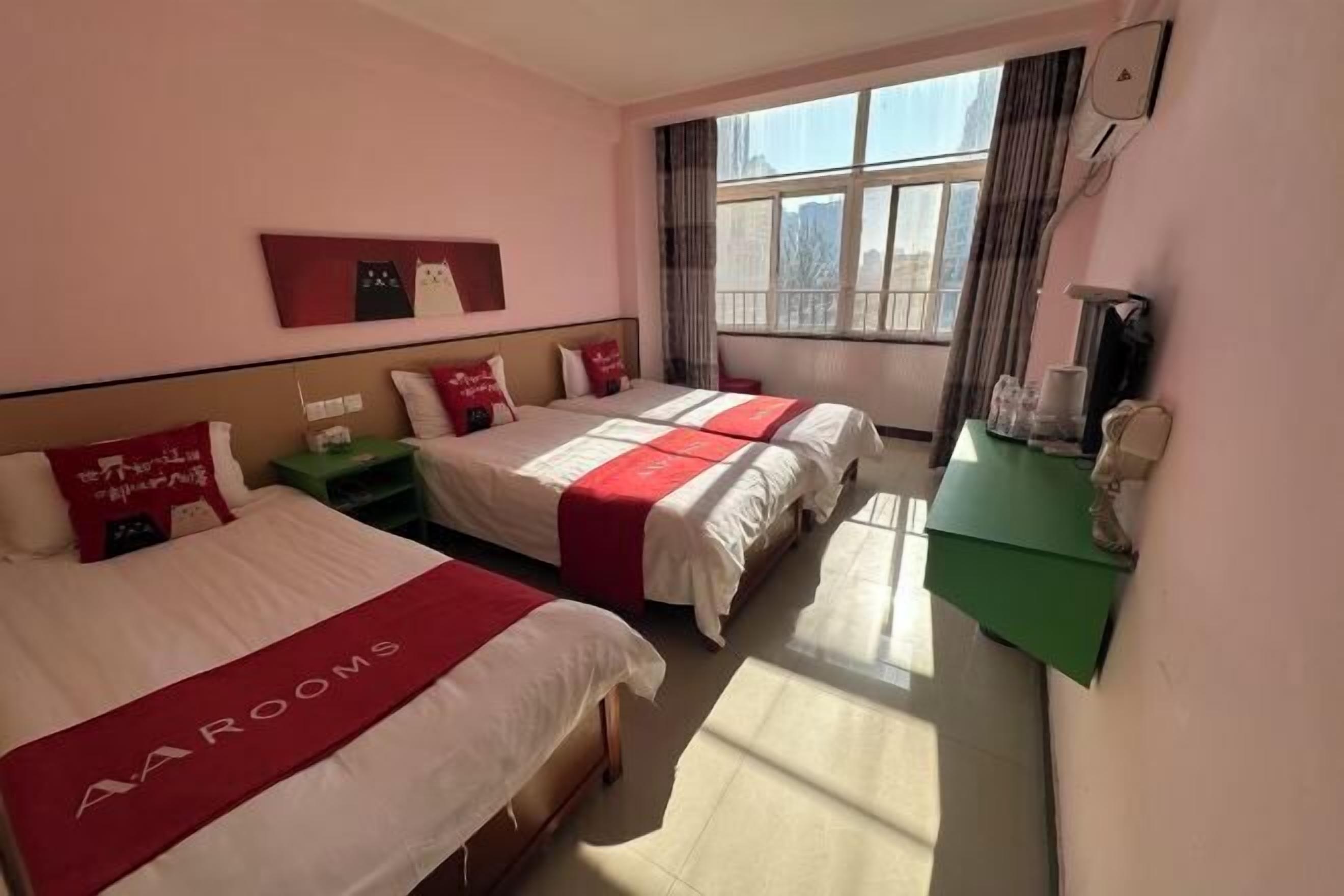 A hotel room with two beds, a green nightstand, a desk, and a large window with curtains.