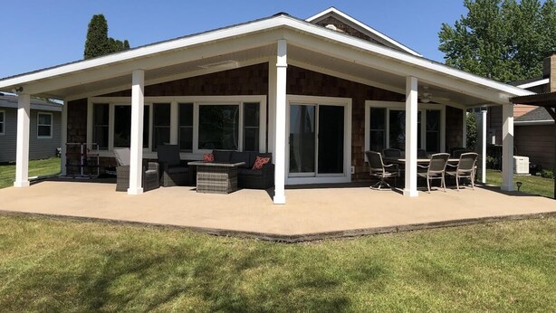 Eine überdachte Terrasse mit Gartenmöbeln, großen Fenstern und einer Außenwand aus Stein.