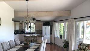 Ein geräumiges Wohnzimmer mit Essbereich, Holzböden, Deckenventilator und großen Fenstern.