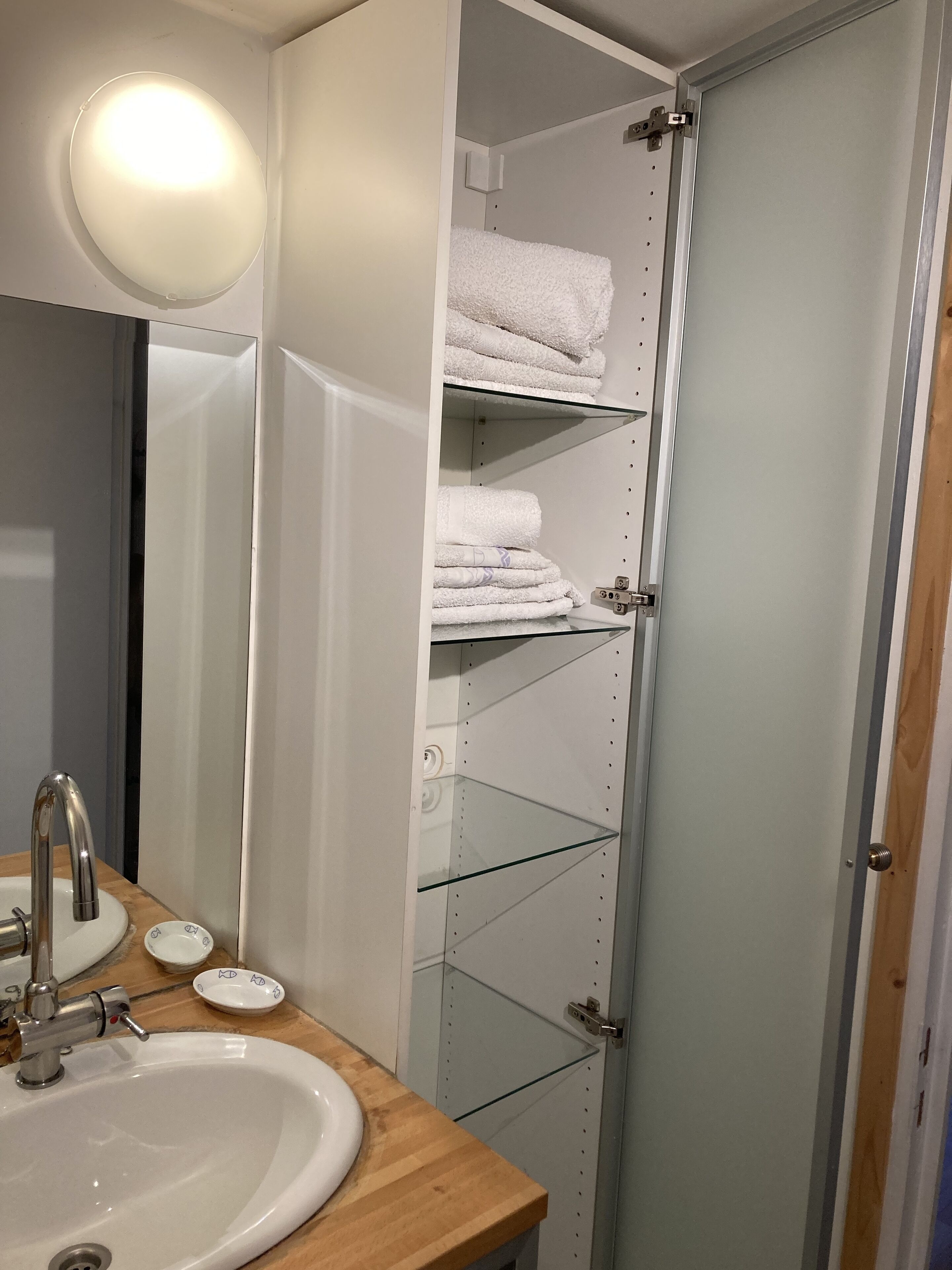 Un baño con un lavabo blanco, un espejo y estantes con toallas dobladas.