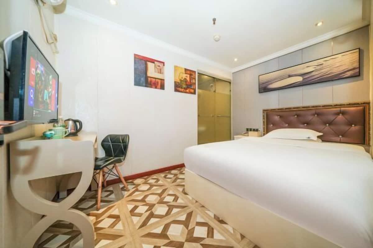 Een hotelkamer met een bed, een bureau met een computer, een stoel en kunstwerken aan de wanden.