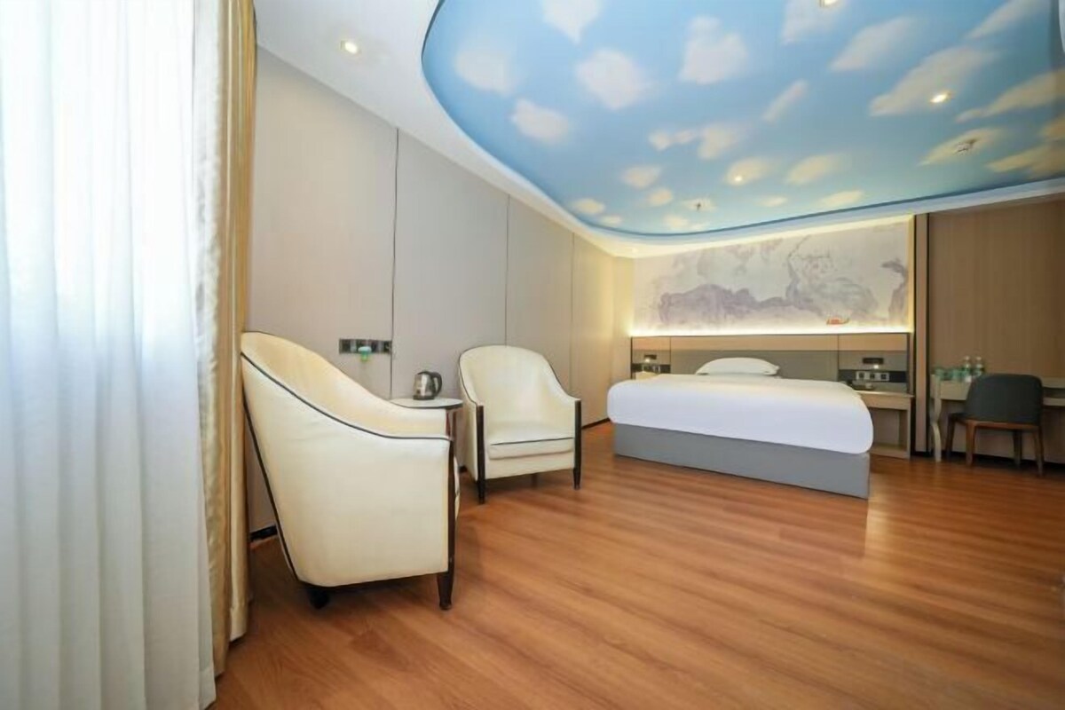 Une chambre d’hôtel moderne avec un plancher en bois, un lit, deux chaises, un bureau et un plafond décoré de motifs nuageux.