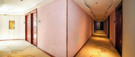A hotel corridor with a carpeted floor, doors on both sides, and a light source at the end.