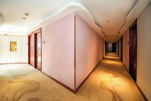 Un corridoio di un hotel con pavimento tappezzato, porte su entrambi i lati e una fonte di luce in fondo.