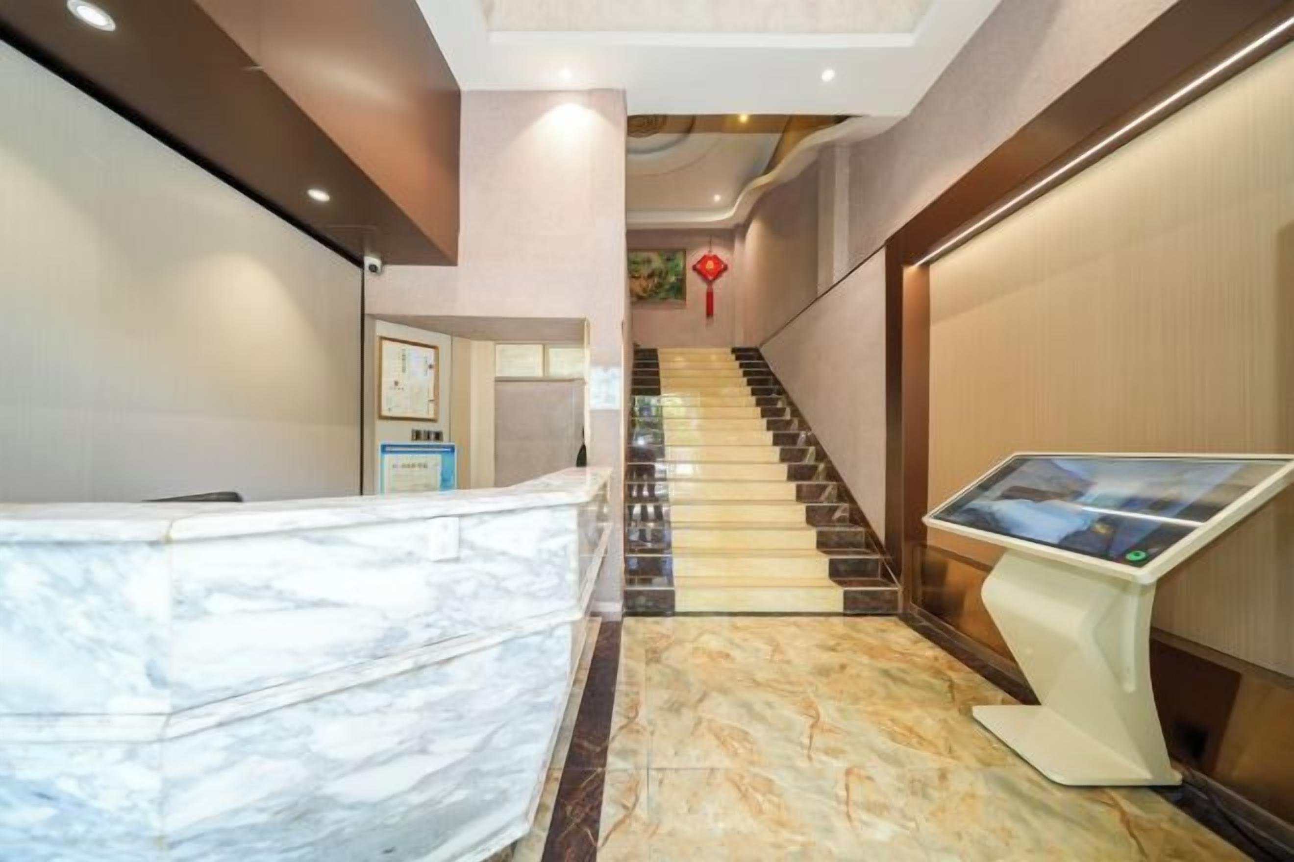 Un hall de hotel con un mostrador de recepción de mármol, un quiosco digital de información y una escalera.