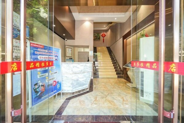 Eine Hotelhalle mit Empfangsschalter, Treppe und Glaswänden.
