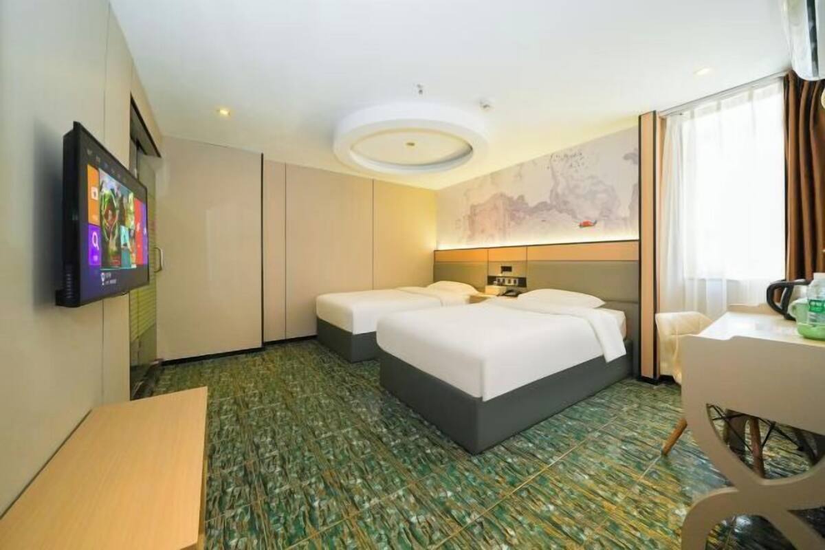 Een hotelkamer met twee bedden, een televisie, een bureau en een groot raam.